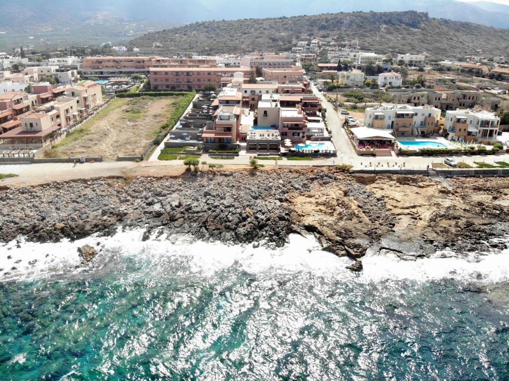 Krasta ainava ar viesnīcām un peldbaseiniem, kas atrodas blakus jūrai, ar akmeņainu piekrasti un kalniem fona.