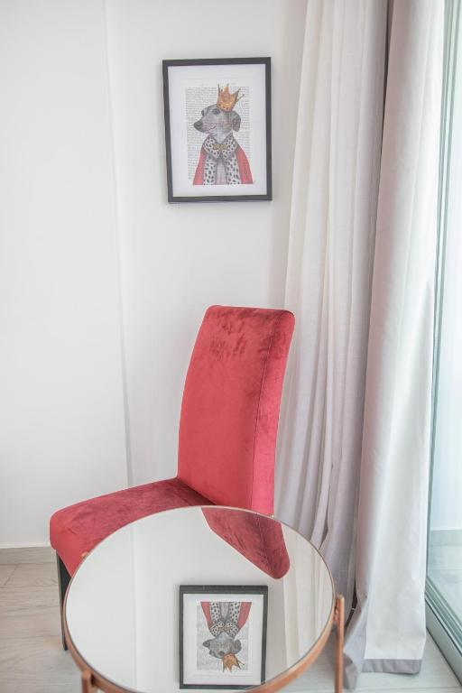 Sarkans krēsls ar apaļu galdu un māksliniecisku attēlu uz sienas, kurā attēlots karalisks dzīvnieks.