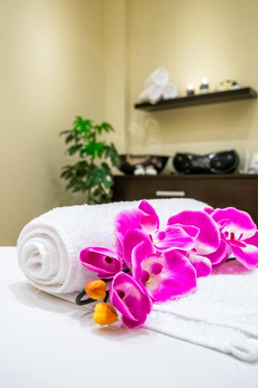 Balts dvielis ar rozā orhidejām un ziediem, kas novietots uz masāžas galda relaksējošā spa vidē.