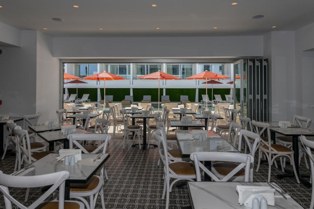 Moderns restorāns ar baltām krēsliem un galdiem, kas piedāvā skatu uz ārējo terasi ar oranžiem saulessargiem. 
