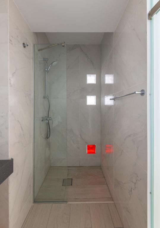 Mūsdienīga duša ar stikla durvīm un marmora flīzēm, nodrošinot elegantu un minimālistisku izskatu. Sarkanā un caurspīdīgā stikla elements piešķir telpai unikālu akcentu.