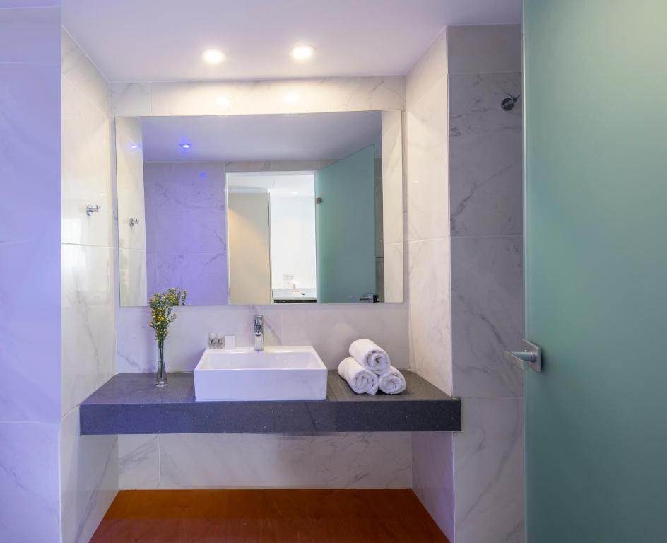 Mūsdienīgs vannas istabas interjers ar pelēku marmora un zaļganu stikla elementiem, kurā redzams izlietne, roku dvieļi un ziedu kompozīcija.