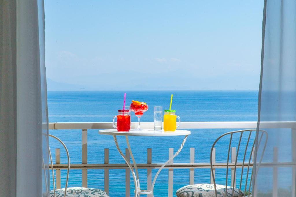 Divi dzērieni uz balkona, skatoties uz zilo jūru. Dzērieni ir spilgti krāsoti, ar salmiņiem un augļiem, radot relaksējošu atmosfēru.