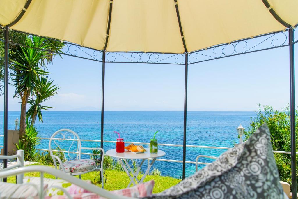 Skaists skats uz jūru no nojumes ar dārza mēbelēm, uz galda atrodas dzērieni un uzkodas, apkārt zaļa zāle un palmas.