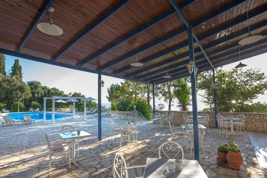 Pastaiga zem jumta ar skatu uz baseinu, kurā ir balti dārza krēsli un galdi, kā arī zaļumi un palmītes. Ideāla vieta relaksācijai un atpūtai.