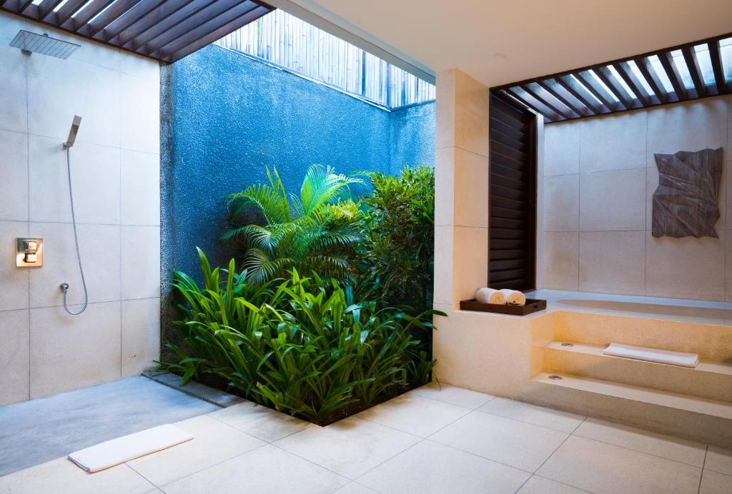 Mūsdienīga vannas istaba ar dušu un zaļu augu stūri, kas rada relaksējošu atmosfēru. Gaisma un dabiskie materiāli piešķir telpai eleganci.