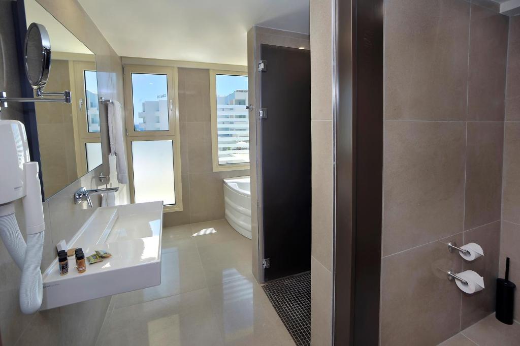 Mūsdienīgs vannas istabas interjers ar lieliem logiem, vannu un dušu, kas nodrošina daudz gaismas. Vannas istabā ir moderna izskata izlietne un higiēnas piederumi.