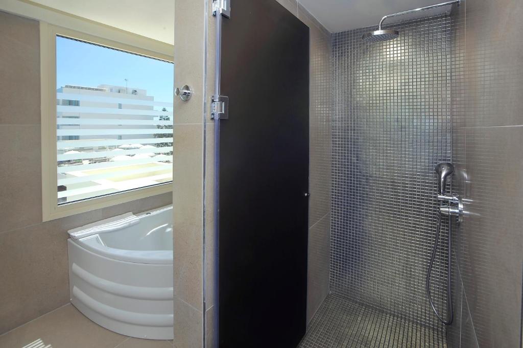 Mūsdienīgs vannas istabas interjers ar dušu un vannu, kas piedāvā lielisku skatu caur logu. Eleganta flīžu apdare un minimālisma dizains rada relaksējošu atmosfēru.