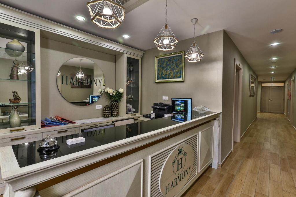 Recepcijas zona ar elegantu dizainu, kurā redzams "Harmony" logo, ziedi un mākslas darbi uz sienām. Gaismas ķermeņi piešķir siltu atmosfēru.
