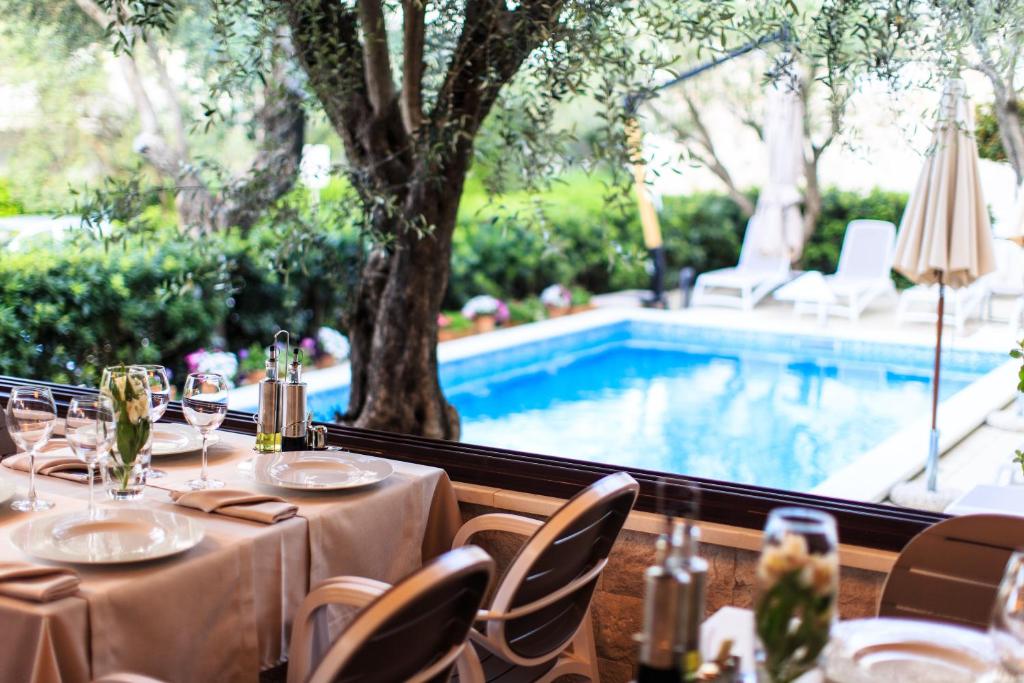 Restorāna galdi ar skatu uz baseinu, apkārtne ar zaļumiem un ziediem, radot relaksējošu atmosfēru.