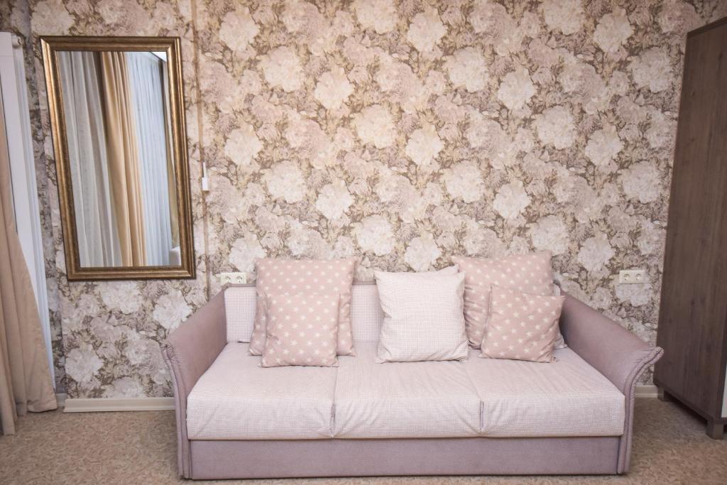 Mūsdienīgs viesistabas interjers ar rozā dīvānu un spilveniem, kas harmonizē ar ziedu tapetēm. Spogulis un koka skapīša elements piešķir telpai eleganci.