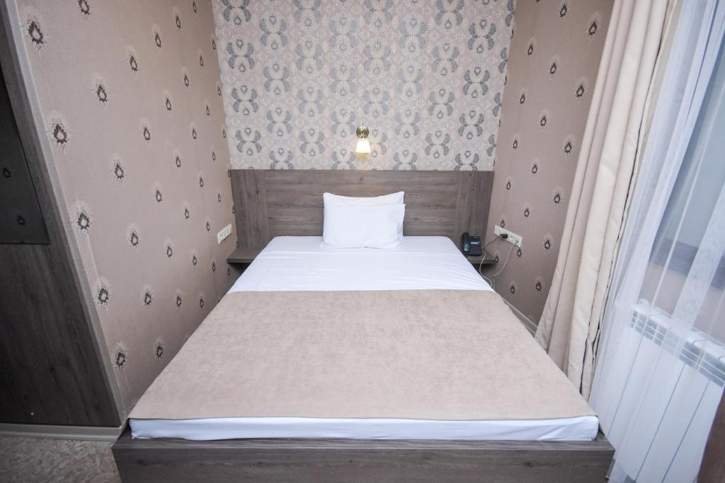 Mūsdienīga viesnīcas istaba ar vienguļamo gultu, dekorēta ar neitrālām krāsām un rakstainām tapetēm. Pie gultas ir naktslampiņa un telefona pieslēgums.