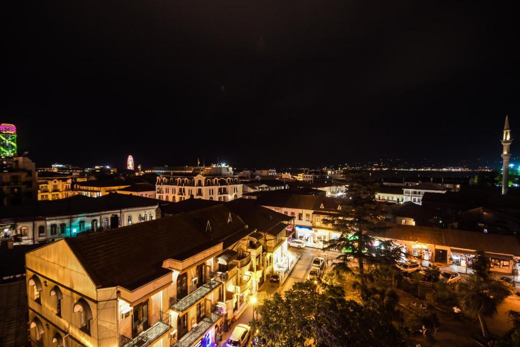 Naktī redzama pilsētas ainava ar apgaismotām ēkām un ielām. Skats uz vēsturisku arhitektūru un mūsdienu gaismas elementiem.