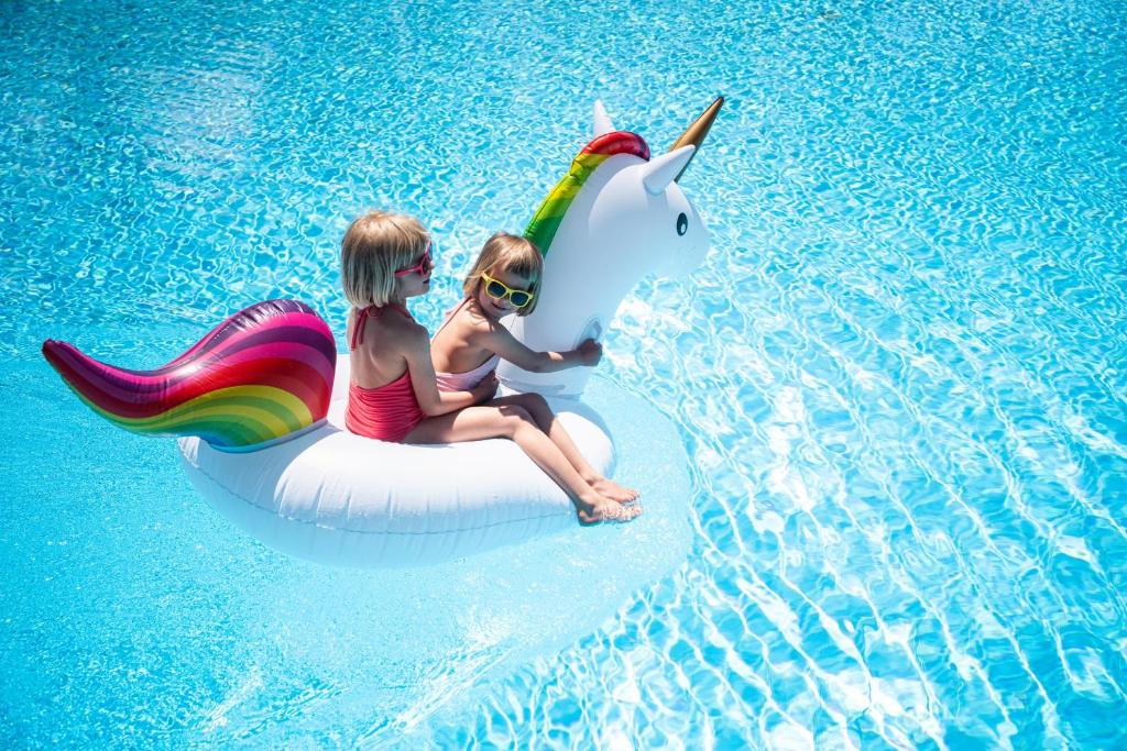 Divas meitenes spēlējas uz pūšamā vienradža peldspēka baseinā, baudot vasaras sauli un jautrību.