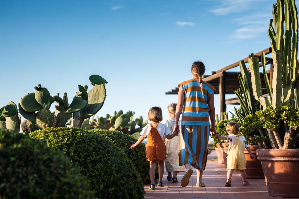 Bērni un pieaugušais soļo pa takti, ko ieskauj kaktusi un zaļumi, baudot saulainu dienu. Šis attēls atspoguļo ģimenes laiku un dabu.