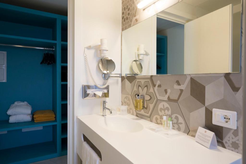 Moderns vannas istabas interjers ar gaišu izskatu, kas ietver spoguli, higiēnas piederumus un krāsainu skapīti. Stūris ar tīrām, salocītām dvieļiem un trauku nodrošina komfortu.