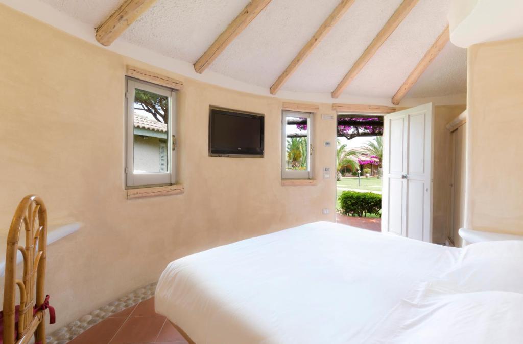 Mūsdienīga guļamistaba ar koka griestiem un logiem, kas paver skatu uz dārzu. Telpā ir ērta gulta un televizors, radot patīkamu un relaksējošu atmosfēru.