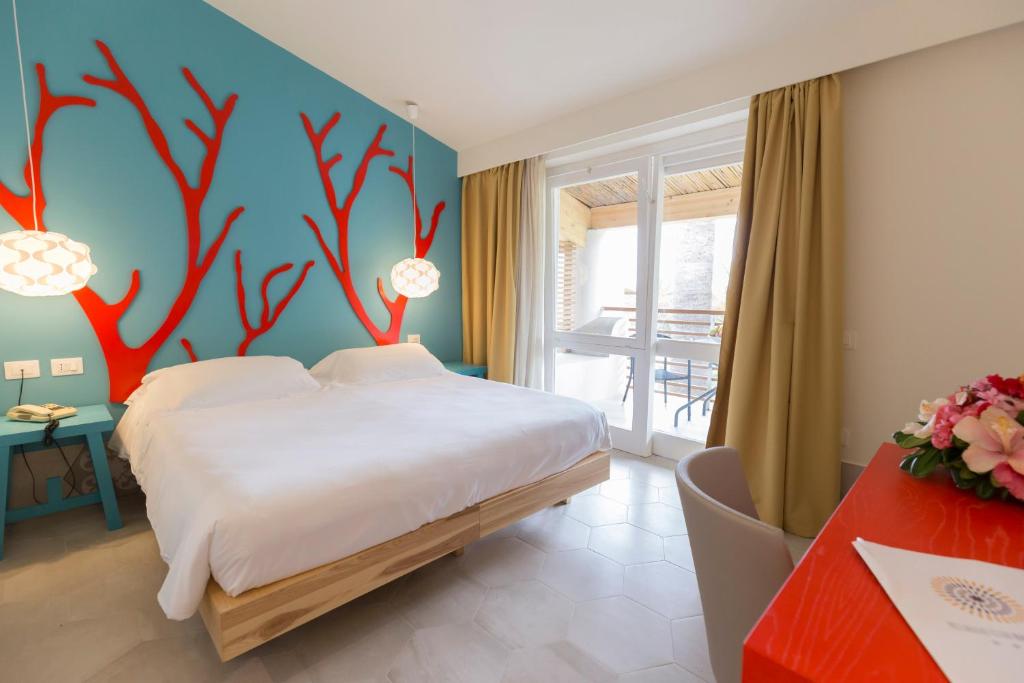 Mūsdienīga viesnīcas numuriņa iekārtojums ar spilgtu zilu sienu un sarkaniem korāļu motīviem. Numurā ir plaša gulta, gaišas aizkaru un mēbeļu krāsas, kā arī balkons ar skatu.