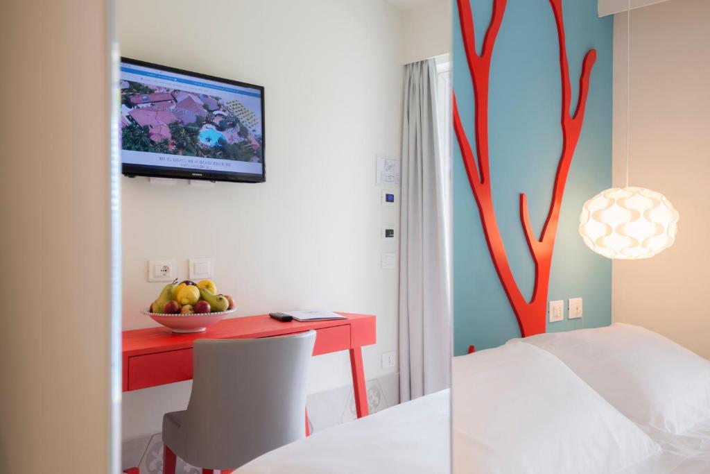 Mūsdienīga viesnīcas numura interjers ar gaišām krāsām, sarkanā galda un krēsla komplektu, televizoru un augļu trauku. Pievilcīgs sienas dekors ar zilu un sarkanu krāsu.