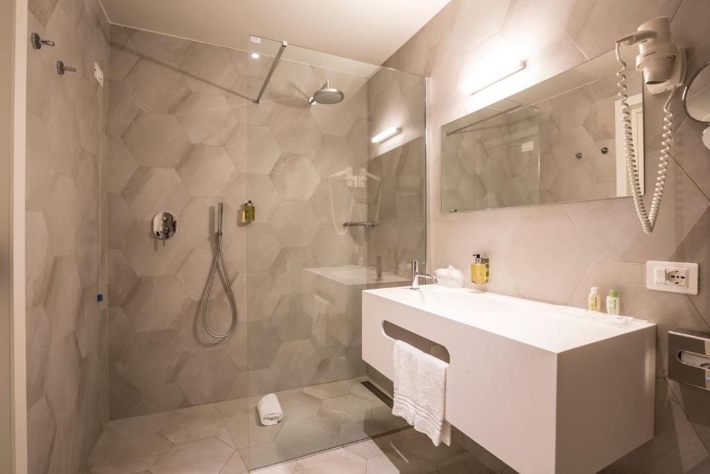 Mūsdienīga vannas istaba ar stikla dušu, pelēkām sešstūra flīzēm un minimālistisku izskatu. Vannas istabā ir moderns izlietnes skapītis un spogulis ar apgaismojumu.