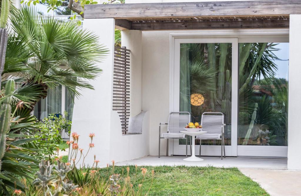 Mūsdienīgs dārza stūrītis ar divām krēslām un galdiņu, uz kura atrodas augļi. Fons ir zaļš ar palmām un citiem augiem, radot relaksējošu atmosfēru.