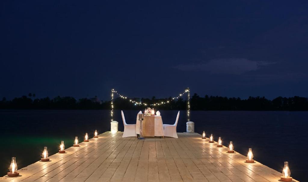 Romantisks galdiņš ar sveču apgaismojumu uz piestātnes pie ūdens, apņemts ar gaismiņām. Ideāli piemērots romantiskām vakariņām.