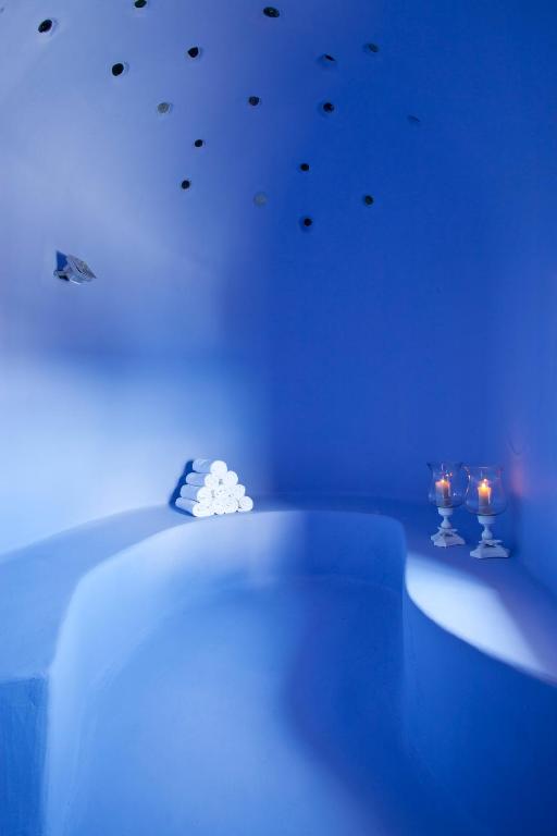 Mierīga un relaksējoša zila telpa ar gludām sienām, uz kurām ir izkārtoti dekoratīvi elementi, un blakus stāv ruļļi dvieļu un sveces.
