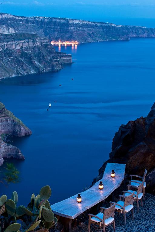 Klusais skats uz jūru un klintīm ar ilgu galdu un laternām, kas veido romantisku atmosfēru. Šī ainava ir ideāla vieta, lai baudītu vakariņas ar skatu uz saulrietu.