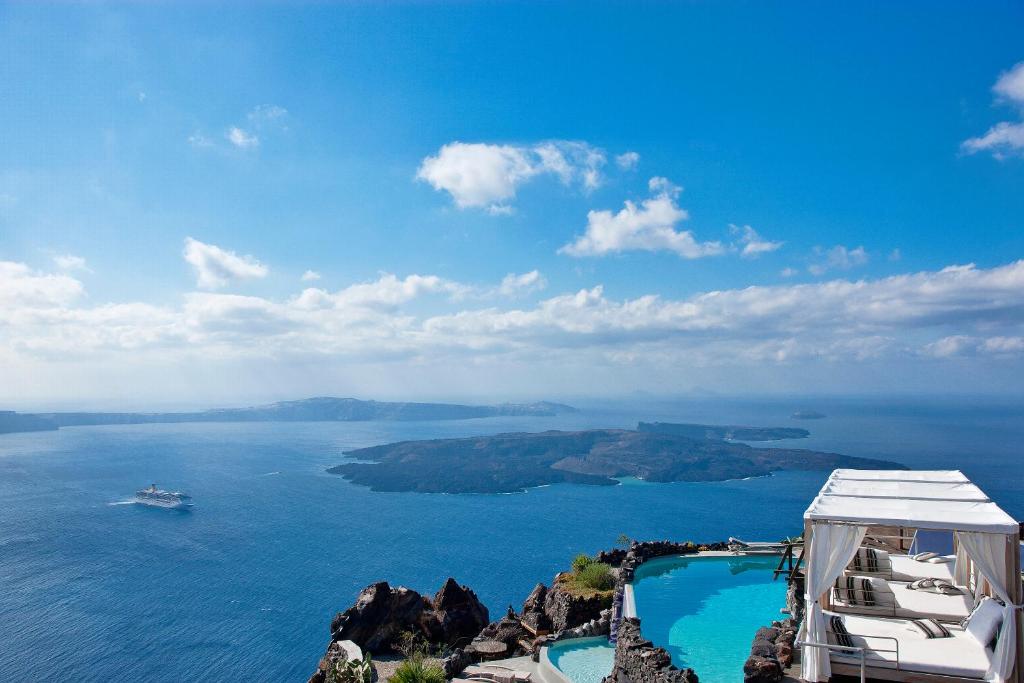 Skaists skats uz jūru un salas ainavu no klints, ar peldbaseinu un atpūtas zonu priekšplānā. Ideāla vieta atpūtai un brīvdienām.