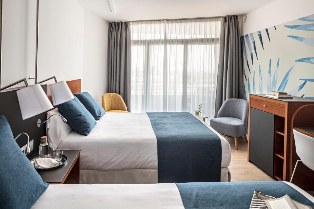 Mūsdienīgs viesnīcas numurs ar divām gultām, gaišām sienām un dabīgu apgaismojumu. Interjerā ir stilīgi mēbeļu elementi un dekoratīvi akcenti.