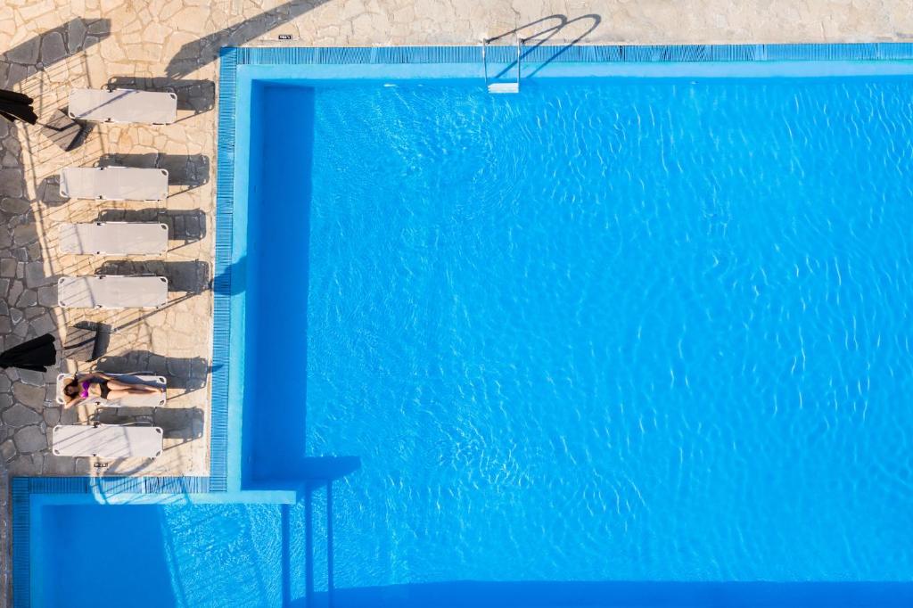 Peldbaseins ar spilgti zilu ūdeni un sauļošanās krēsliem, kuros atpūšas cilvēks. Ideāla vieta relaksācijai un vasaras izbaudīšanai.