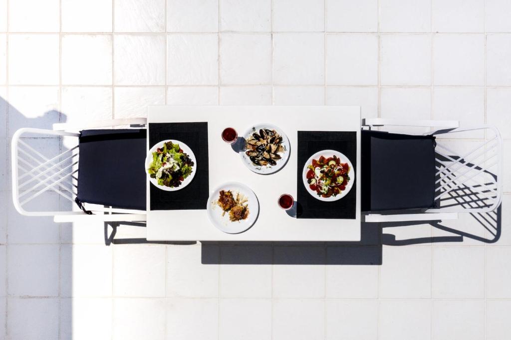 Galds ar dažādām ēdienu porcijām, tostarp salātiem un garnelēm, izvietots uz terases, blakus diviem melniem krēsliem. Ideāla atmosfēra relaksējošai maltītei ārā.