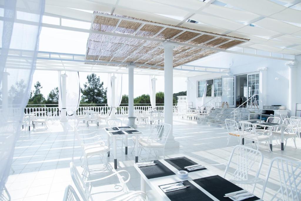 Mūsdienīgs terases restorāns ar baltām mēbelēm un saulainu atmosfēru, ideāli piemērots relaksācijai un maltītēm ārā.