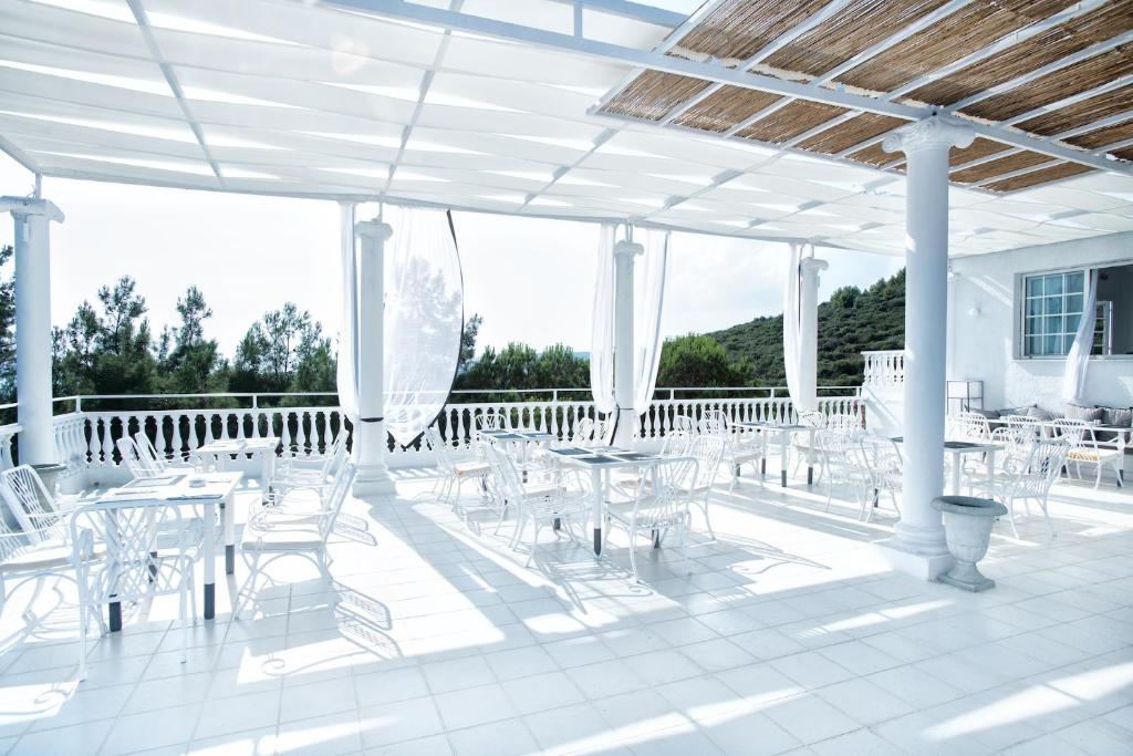 Balta terase ar galdiem un krēsliem, kas atrodas saulainā vietā, ar skatu uz zaļām kokiem un kalniem. Ideāli piemērota relaksācijai un ēdienošanai ārā.