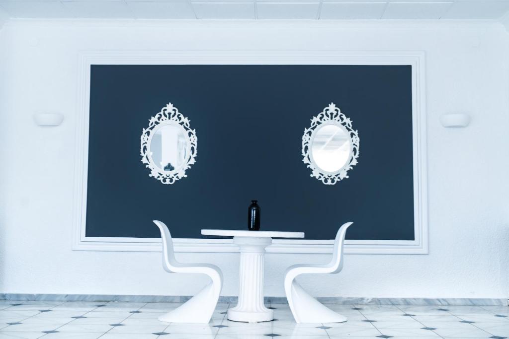 Mūsdienīga interjera dizaina telpa ar baltām krēsliem, apaļu galdu un melnu vāzi, kas izceļas uz tumši zila fona ar divām elegantiem spoguļiem.