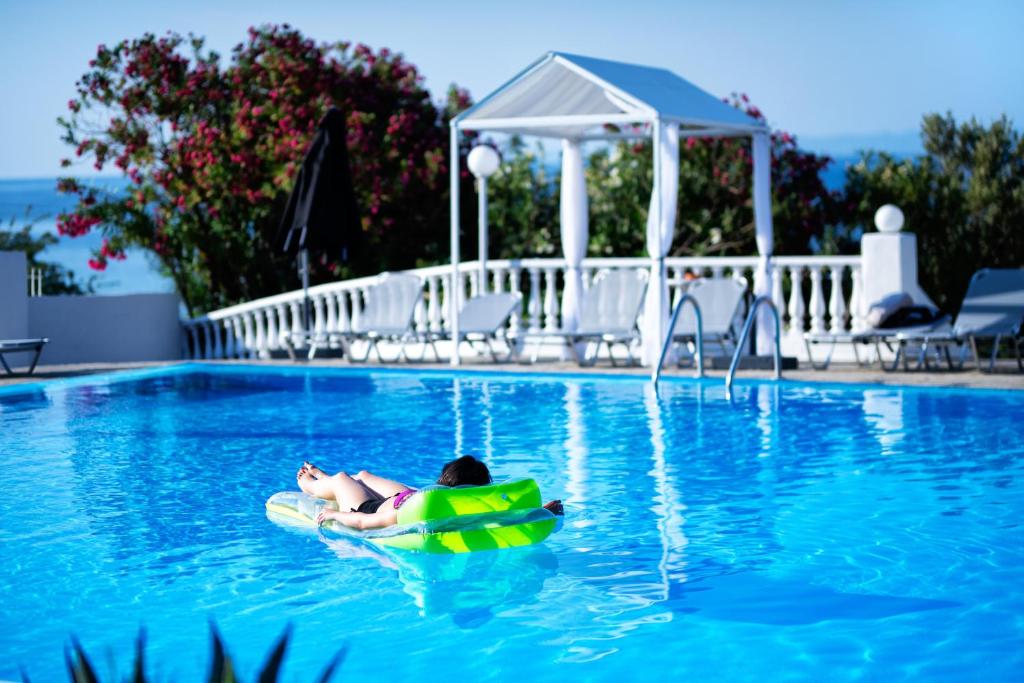 Svaigā zila baseina ainava ar cilvēku, kas relaksējas uz piepūšamā pludiņa. Apkārt ir saulaini laika apstākļi un skaisti ziedi.