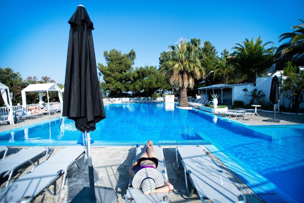 Peldbaseins ar sauļošanās krēsliem un palmām, ideāla vieta atpūtai, ar skaidru zilu debesi fonā. Relaxing atmosphere by the poolside.