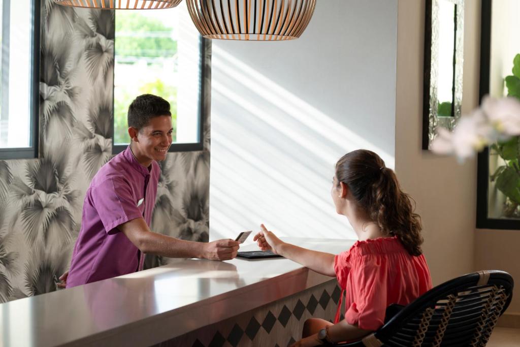 Reģistratūras darbinieks laipni apkalpo viesi, nododot viņai karti. Interjers ir moderns ar pievilcīgu dizainu.