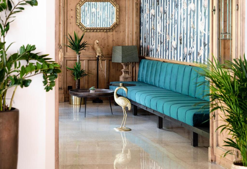 Mūsdienīgs interjers ar zaļo dīvānu, stilīgu galdu un dekoratīvām augiem, radot relaksējošu atmosfēru. Ievērojama ir arī apdare ar putnu motīviem uz sienas.