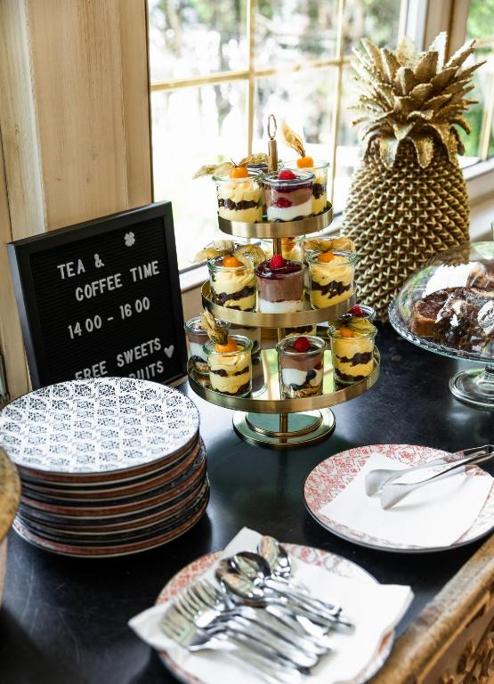 Teātra un kafijas stunda ar gardiem desertiem, kas izkārtoti eleganti uz vairāku līmeņu stenda. Klātas krāšņas šķīvju un galda piederumu komplekti.