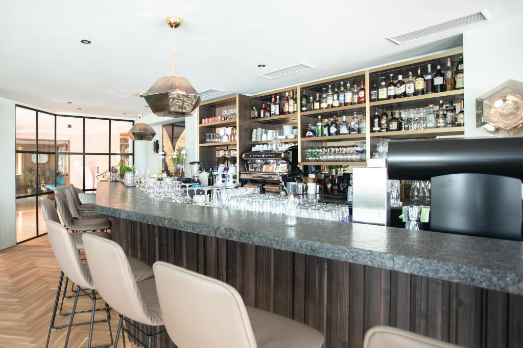 Mūsdienīgs bārs ar elegantu dizainu, kurā redzama gluda akmens virsma un plaša dzērienu izvēle uz plauktiem. Interjerā ir komfortablas krēsli un daudz gaismas.