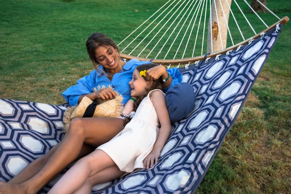Sieviete un bērns atpūšas šūpuļtīklā Desert Rose Resort dārzā.