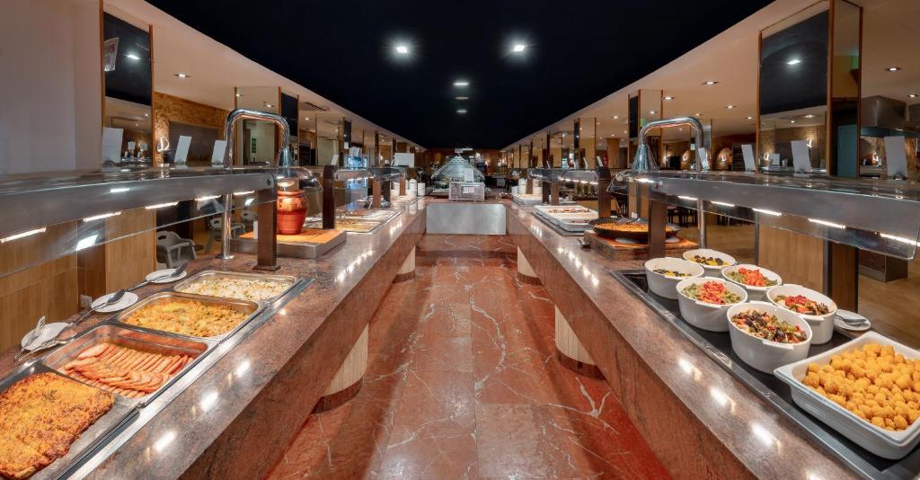 Bufete ar plašu ēdienu izvēli, ietverot karstos ēdienus un salātus, modernā restorānā. Elegants interjers ar apgaismojumu un marmora virsmām.