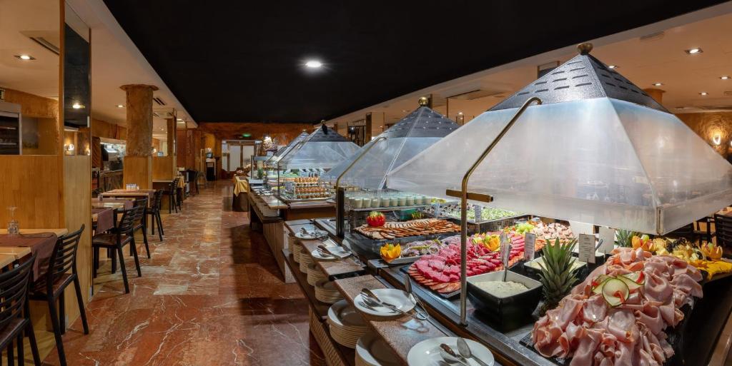 Restorāna interjers ar bufeti, kurā redzami dažādi ēdieni, tostarp augļi un gaļa, apgaismots ar siltām gaismām. Elegants un aicinošs atmosfēra.