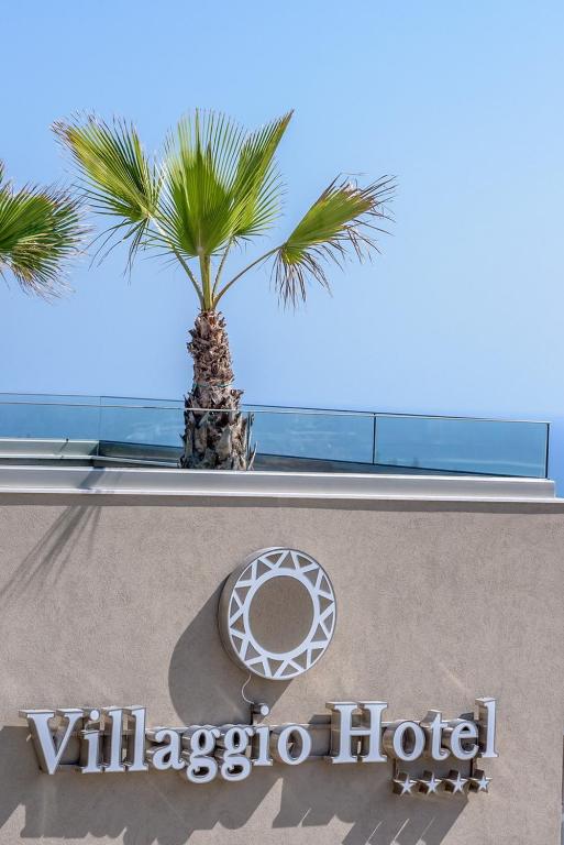 Villaggio Hotel zīme ar palmu fona un skaidru debesu, kas rada viesmīlīgu atmosfēru.