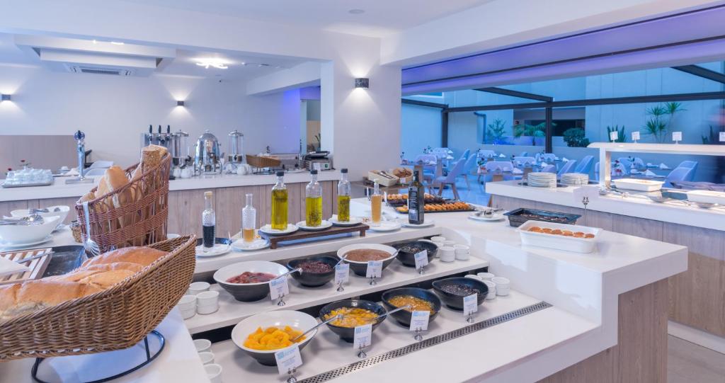 Brokastu bufete ar dažādiem ēdieniem, tostarp maizi, eļļu un augļiem, iekārtota modernā telpā ar gaišām krāsām un elegantu dizainu. Svaigi pagatavoti ēdieni un patīkami interjers padara šo vietu pievilcīgu.