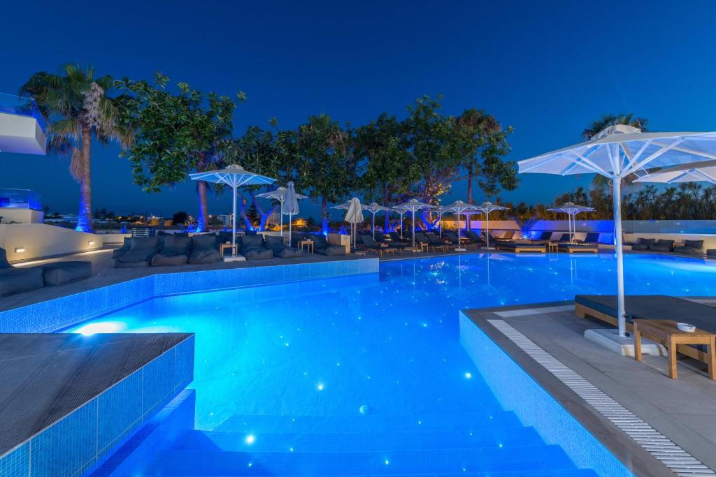 Mūsdienīgs baseins ar spilgti zilu ūdeni, apkārt palmām un sauļošanās krēsliem, kas apgaismoti nakts laikā. Relaksējoša atmosfēra ar elegantiem saulessargiem un mūsdienīgu dizainu.
