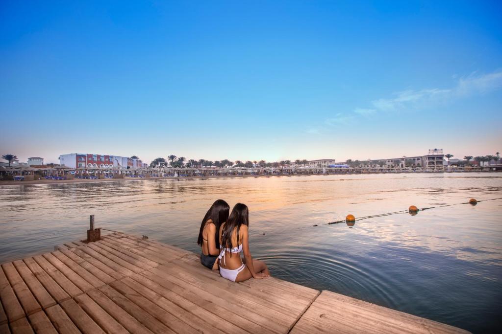 Divas meitenes sēž uz platformas piekrastē, vērojot saulrietu pie Sunrise Garden Beach Resort.