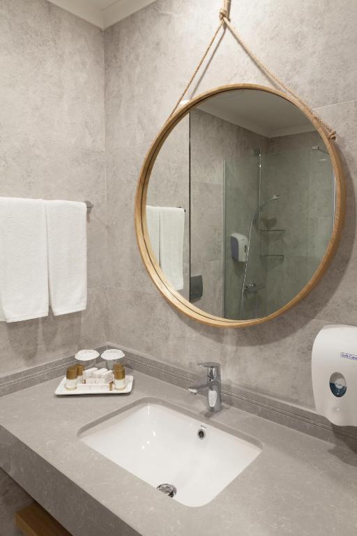 Mūsdienīgs vannas istabas interjers ar apļveida spoguli un elegantu izlietni. Uz galda atrodas kosmētikas līdzekļi un dvieļi, radot relaksējošu atmosfēru.