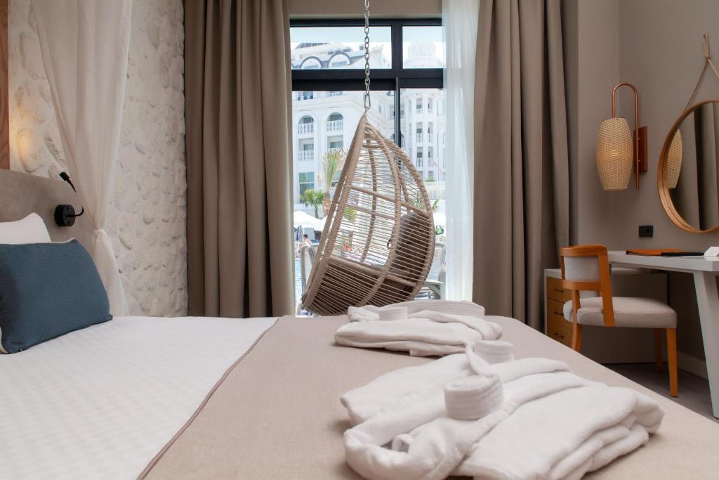 Mūsdienīgs viesnīcas numurs ar ērtu gultu, šūpuļkrēslu pie loga un elegantu interjeru. Gaisma plūst cauri logiem, radot relaksējošu atmosfēru.